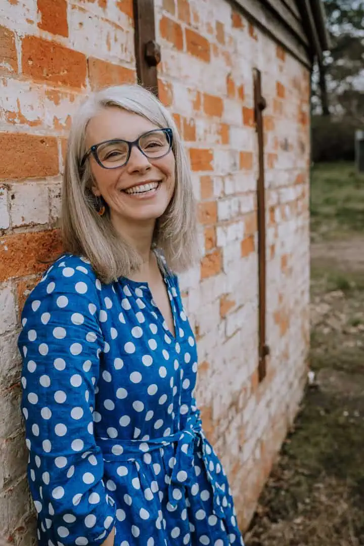 Photograph of Asha Hudson wearing a blue dress leaning on a brick wall smiling